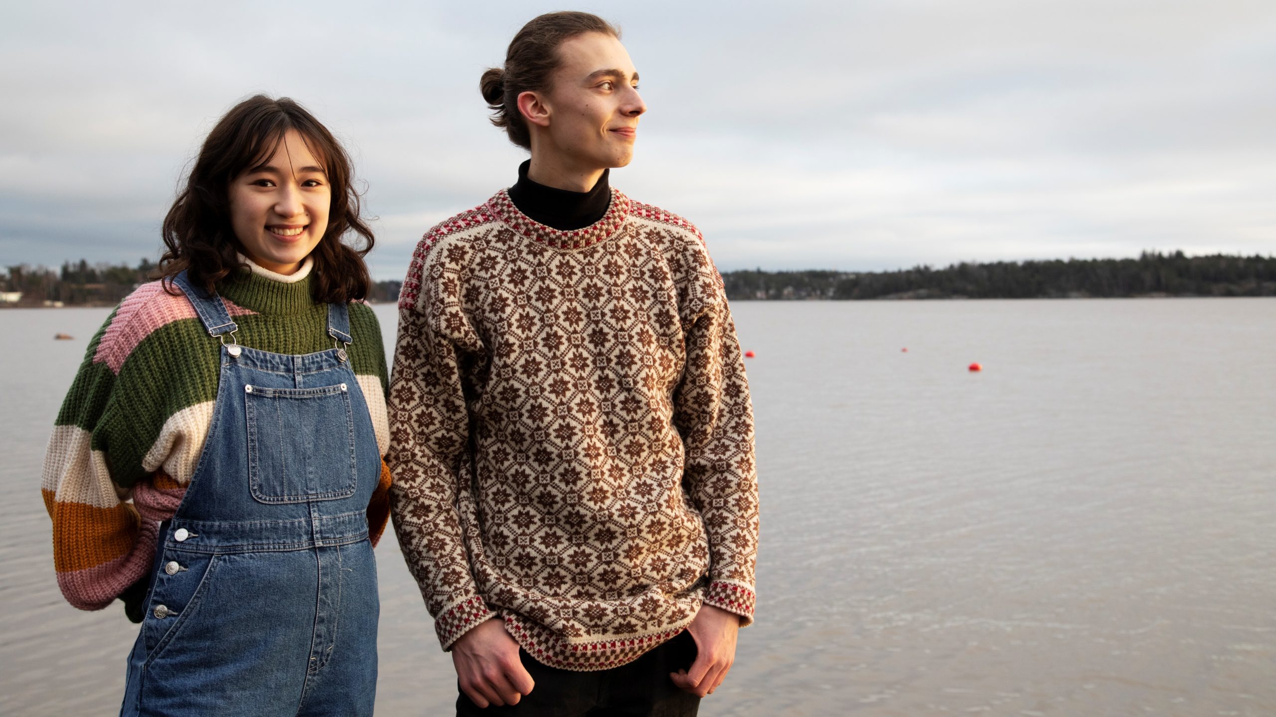 Nainen ja mies seisovat vierekkäin hymyillen järven rannalla.