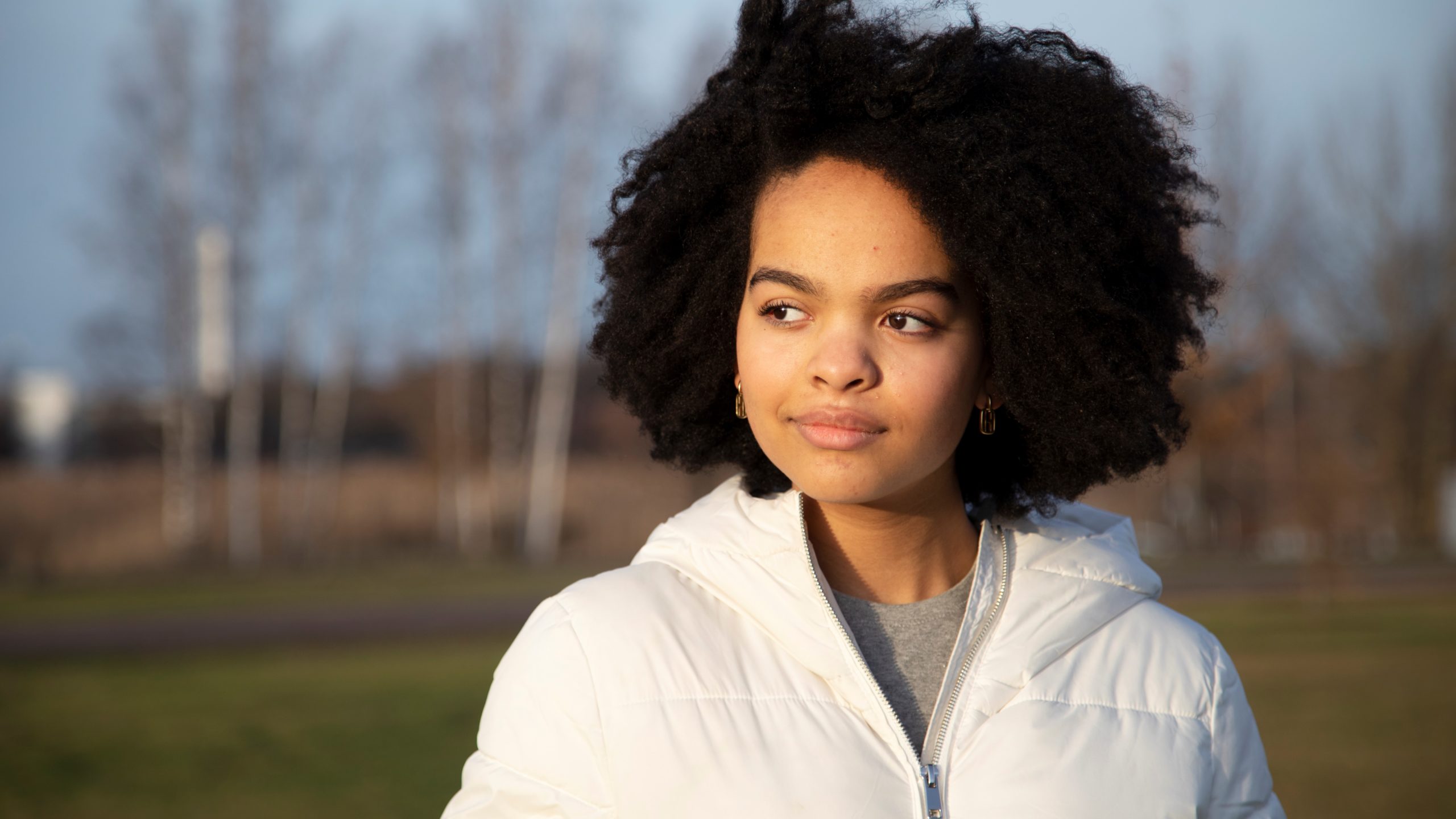 Nuori nainen ulkoiluvaatteissa katsoo sivuun kohti auringonpaistetta.
