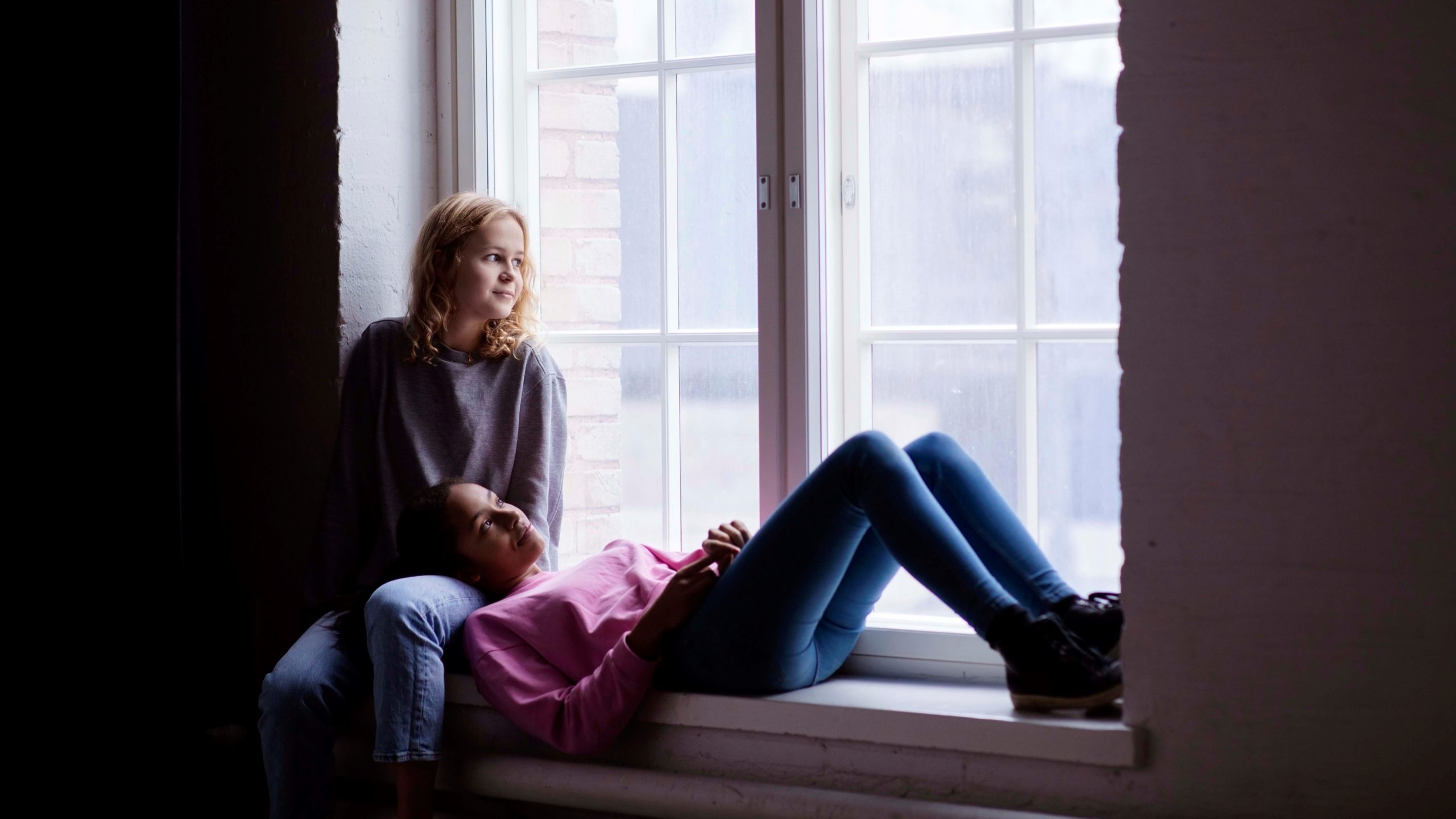 Kaksi rauhallisen oloista nuorta lähekkäin ikkunalaudalla katselevat ulos.