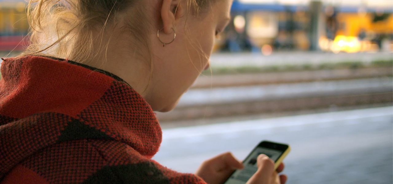 Kaupungilla nuori nainen katsoo alas kohti puhelintaan, jonka näyttö näkyy vilaukselta.
